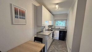 Een compacte keuken met witte kastjes, een houten eettafel en een raam dat natuurlijk licht binnenlaat.