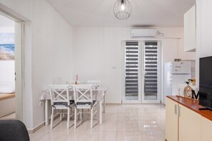 Een moderne keuken met een ingebouwde oven, een eethoek met een tafel en stoelen, en uitzicht op zee door een schuifdeur.