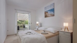 A bedroom with a bed, a nightstand, a lamp, and a painting of a beach scene. - Sea View Apartment Terazza Grande, Selce, Croatia (Selce)
