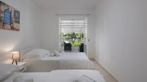 A bedroom with two beds, a window with a view of greenery, a painting on the wall, and a bedside lamp. - Sea View Apartment Terazza Grande, Selce, Croatia (Selce)