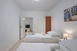 Ein Hotelzimmer mit zwei Betten, einer Holztür, einem Gemälde, einer Lampe und einem Fernseher im Hintergrund.