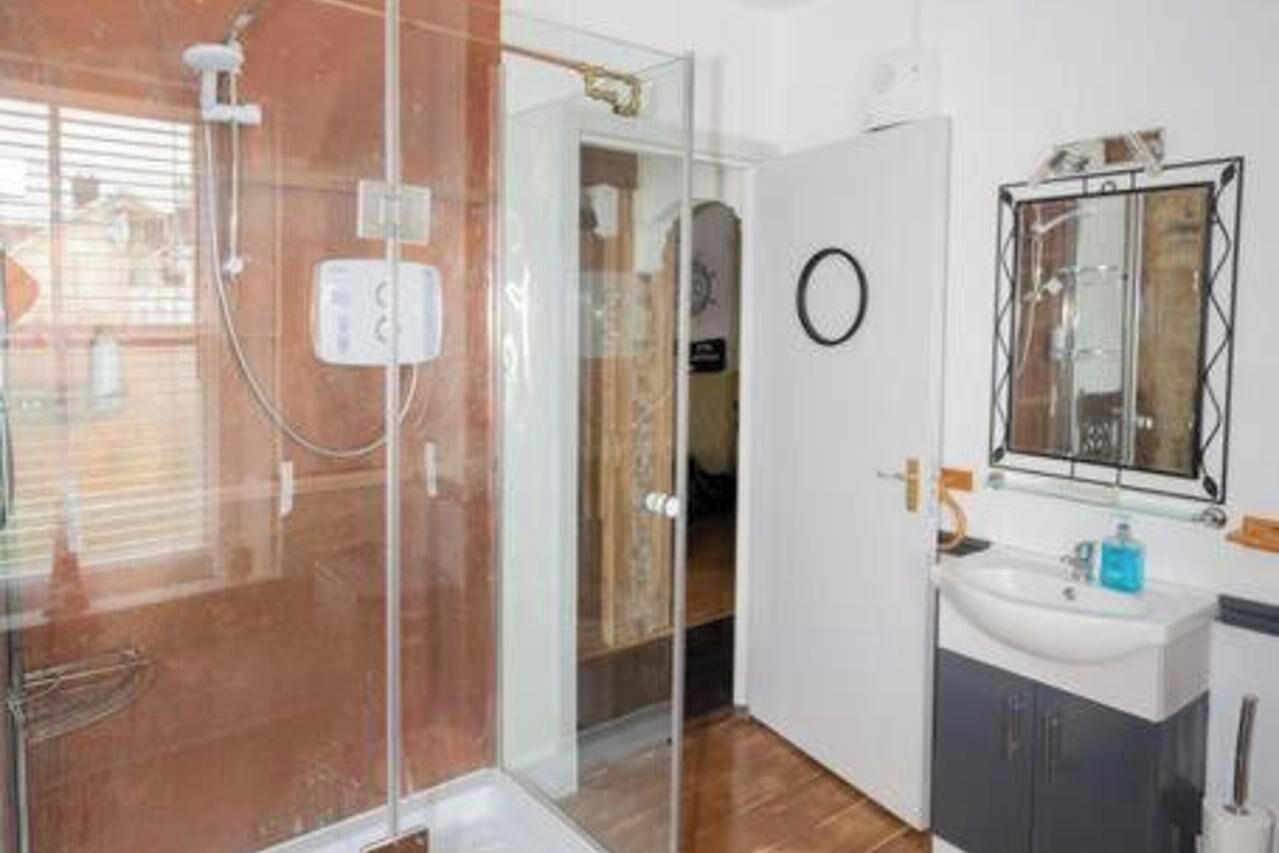 A modern bathroom with a glass shower enclosure, a sink with a mirror, and wooden flooring.