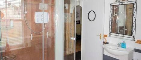 A modern bathroom with a glass shower enclosure, a sink with a mirror, and wooden flooring.