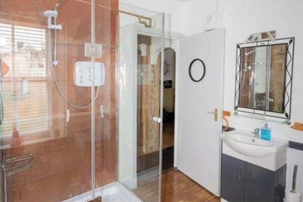 Un baño moderno con cabina de ducha de vidrio, un lavabo con espejo y suelo de madera.