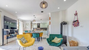 A modern living room with yellow and green chairs, a grey sofa, and a small table. There is a kitchen in the background with a dining area.