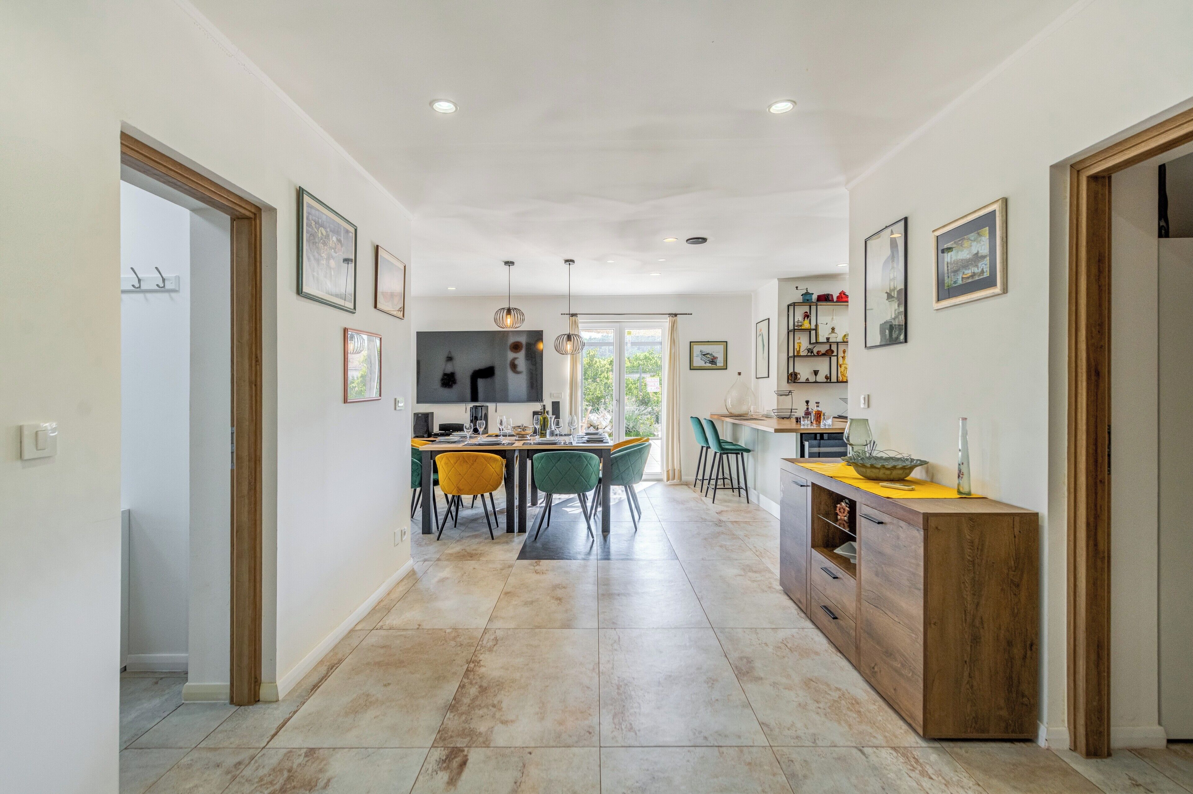 A modern kitchen with a dining area, featuring a central island, pendant lighting, and a view to the outdoors.