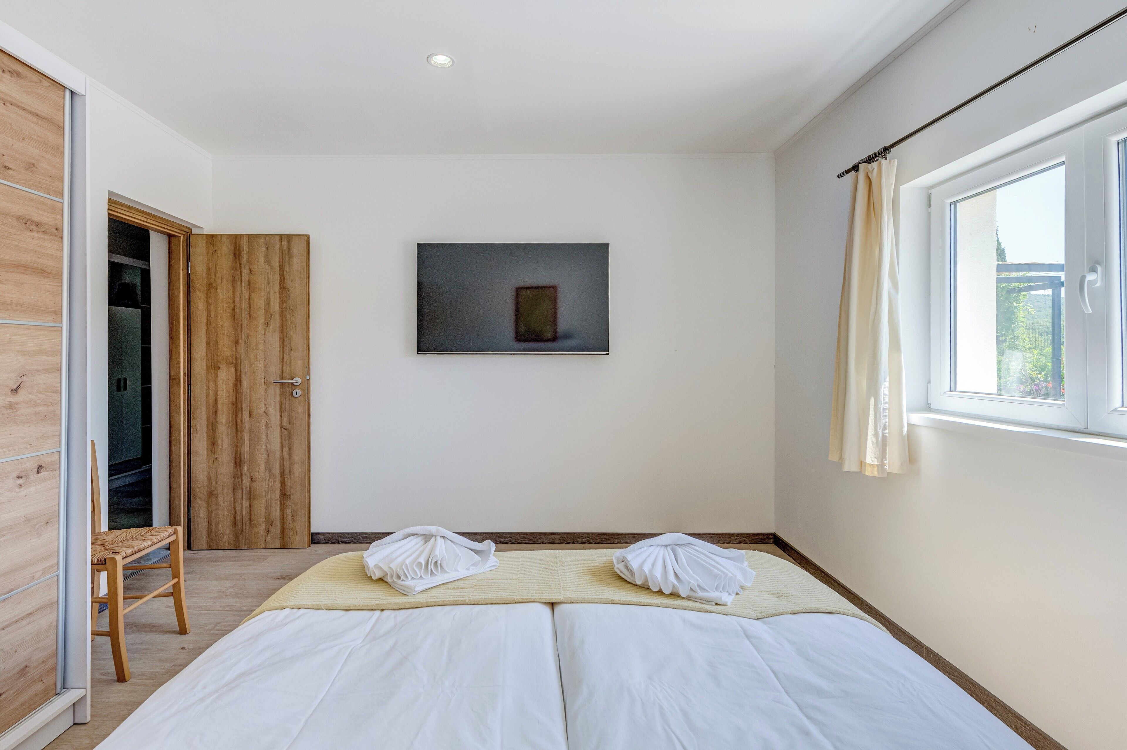 A bedroom with a bed, a wooden wardrobe, a framed picture on the wall, and a window with curtains.