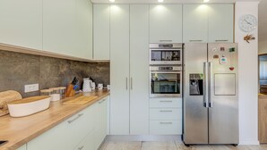 A modern kitchen with white cabinets, a stainless steel refrigerator, an oven, and a wooden countertop.