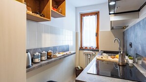A compact kitchen with white tiles, a black countertop, and wooden shelves.