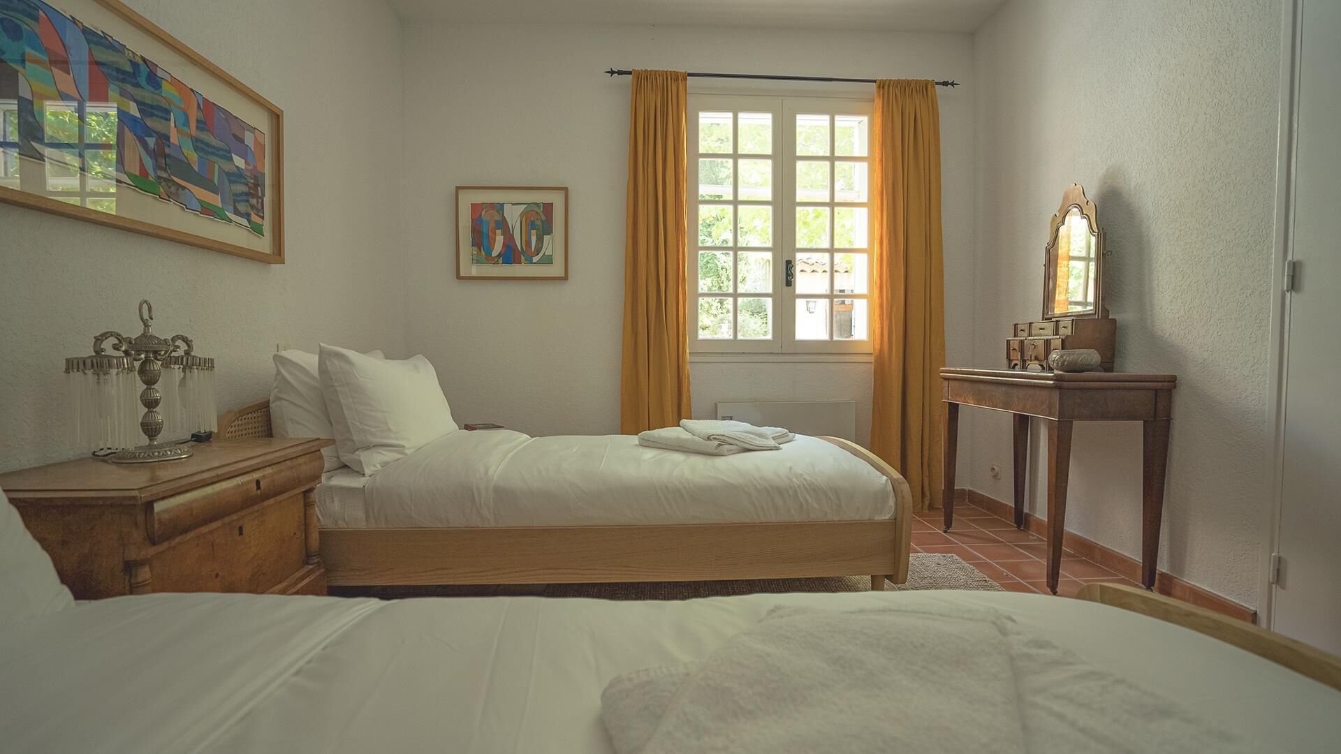 A bedroom with a bed, a bedside table, a dresser, a mirror, and a window with curtains.
