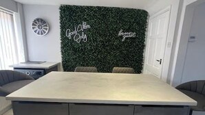 A modern kitchen with a large island, dark green wall decor, and a clock on the wall. - Perfect 3 bedroom home - Contractors & Families (Wolverhampton)