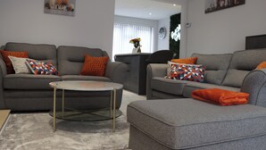 A modern living room with two grey sofas, a round glass coffee table, and orange throw pillows. - Perfect 3 bedroom home - Contractors & Families (Wolverhampton)