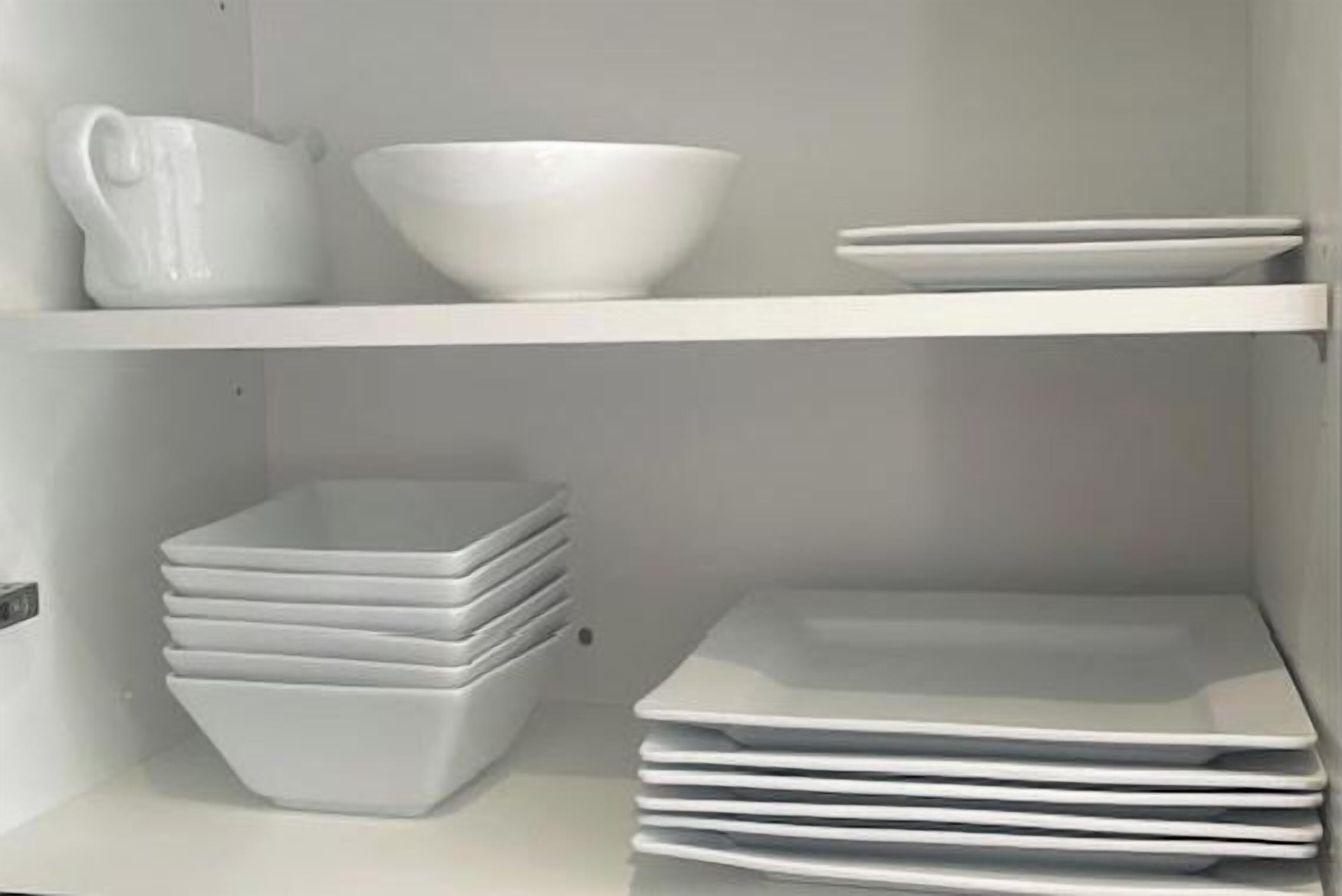 A white shelf with a white pitcher, a white bowl, and a stack of white plates.