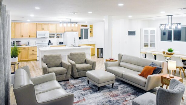 A modern living room with a sofa, armchairs, and ottoman, a kitchen in the background, and a dining area with a table and chairs. - Backyard Oasis - Downtown - Retro Chic - King Bed (Kanab)