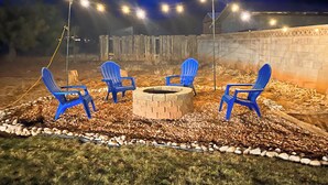 A patio area with four blue chairs arranged around a stone fire pit, surrounded by a gravel and pebbles ground cover. - Backyard Oasis - Downtown - Retro Chic - King Bed (Kanab)