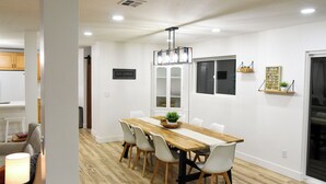 A dining area with a wooden table, white chairs, a hanging light fixture, and a window with a view. - Backyard Oasis - Downtown - Retro Chic - King Bed (Kanab)