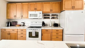A kitchen with wooden cabinets, a microwave, a stove, a refrigerator, and various kitchen appliances. - Backyard Oasis - Downtown - Retro Chic - King Bed (Kanab)