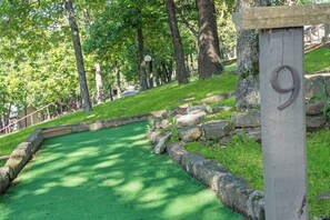 Un parcours de golf avec une surface en gazon synthétique verte, bordé de pierres, et un panneau en bois portant le chiffre 9.