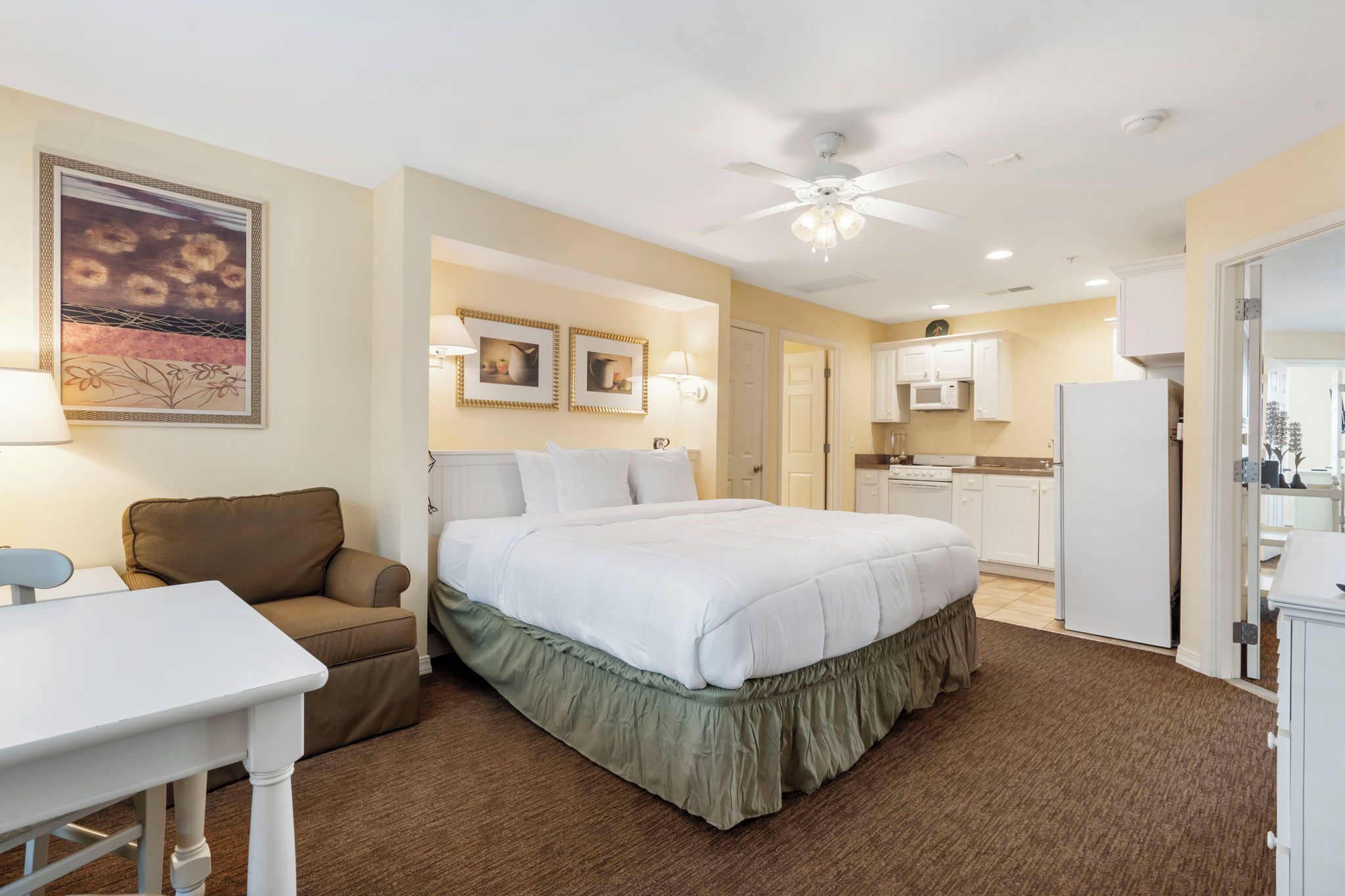 Ein Hotelzimmer mit Bett, Schreibtisch, Stuhl, einer Küchenzeile und einem Deckenventilator.