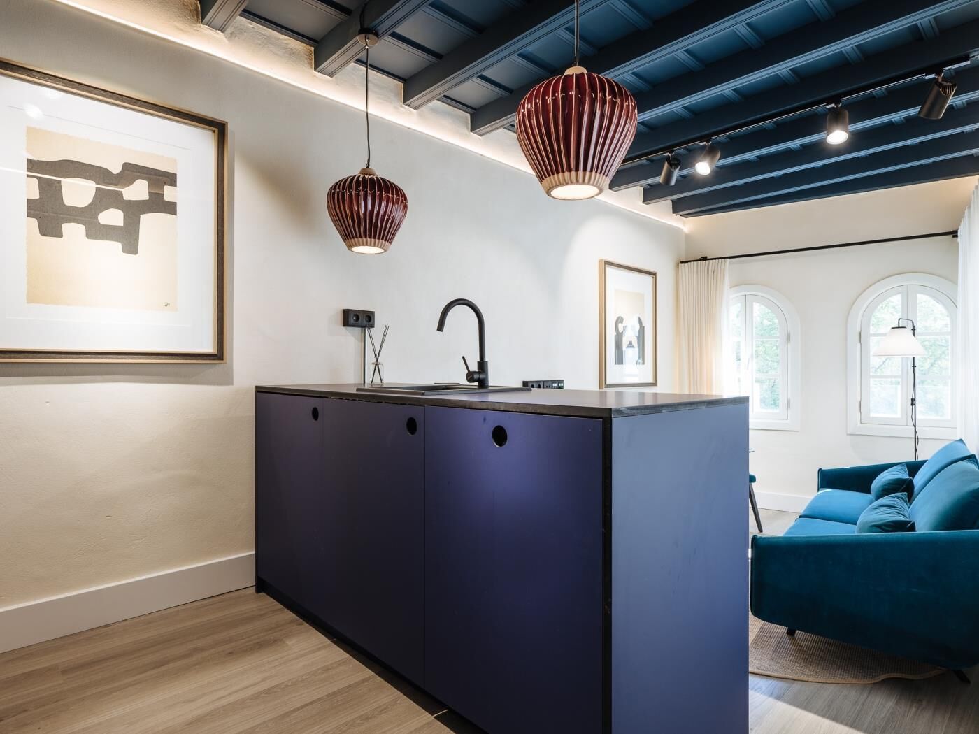 Une cuisine moderne avec un îlot central, des luminaires suspendus et des œuvres d’art accrochées aux murs.