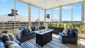A covered outdoor seating area with a fire feature, large windows, and a view of a building with a metal roof.