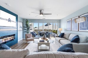 Ein modernes Wohnzimmer mit Kamin, Deckenventilator und großem Fenster mit Blick auf ein Gebäude.