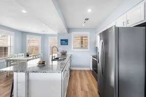 Una cocina moderna con armarios blancos, encimera de granito, refrigerador de acero inoxidable y horno empotrado.