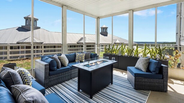 A covered outdoor seating area with a fire pit, sofas, and potted plants.