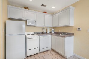 Cocina compacta con electrodomésticos blancos, incluyendo un refrigerador, microondas, estufa y lavavajillas, y un lavamanos con grifo.