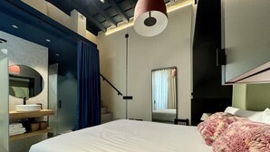 Une chambre d’hôtel moderne avec un grand lit, une table de chevet, un miroir et un luminaire au plafond.