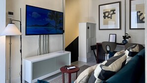 Un salon moderne avec un téléviseur à écran plat, un meuble de rangement blanc, un canapé agrémenté de coussins à motifs, une petite table et un fauteuil.