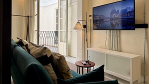 Un salon moderne avec un canapé, un téléviseur fixé au mur et un balcon offrant une vue sur le paysage urbain.