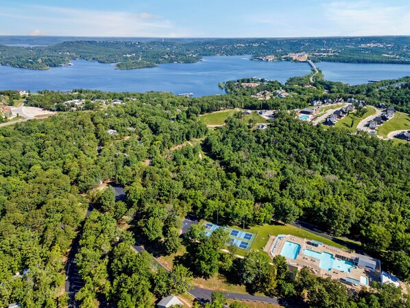 An aerial view of a residential area with a large body of water, dense greenery, and a swimming pool complex.