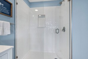 Un bagno moderno con doccia vetrata, piastrelle bianche e una citazione incorniciata al muro.