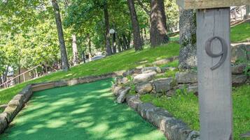 Ein Golfplatz mit künstlichem Rasen, einer Steinmauer und einem Holzschild mit der Aufschrift 9.