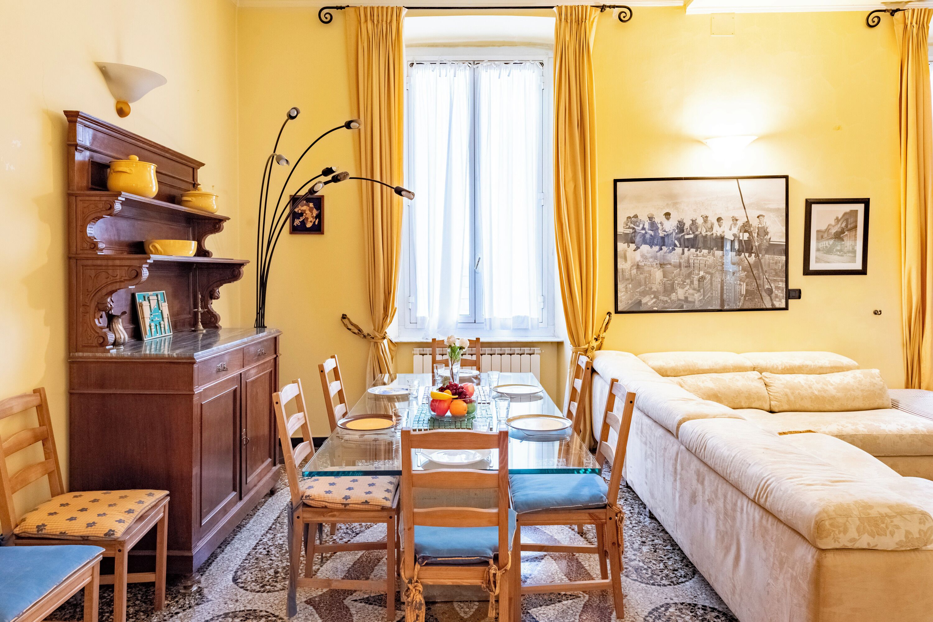 A dining area with a glass table, wooden chairs, a wooden cabinet, and a sofa.