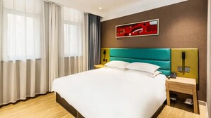 A hotel room with a large bed, a teal headboard, white bedding, a wooden floor, a nightstand with a phone, and a painting on the wall. - Wode  Hotel Tengzhouhuochezhandian (Zaozhuang)