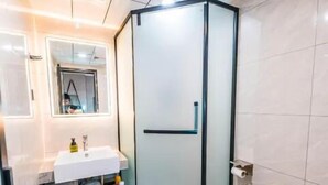 A modern bathroom with a glass shower enclosure, a white sink, and a toilet. - Wode  Hotel Tengzhouhuochezhandian (Zaozhuang)
