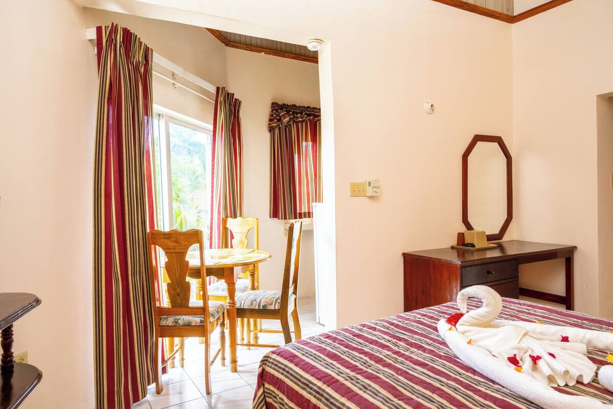 Habitación de hotel con cama, escritorio de madera, silla y ventana con cortinas.