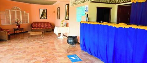 A room with a sofa, a table with a vase, a black pot, and a blue curtain.