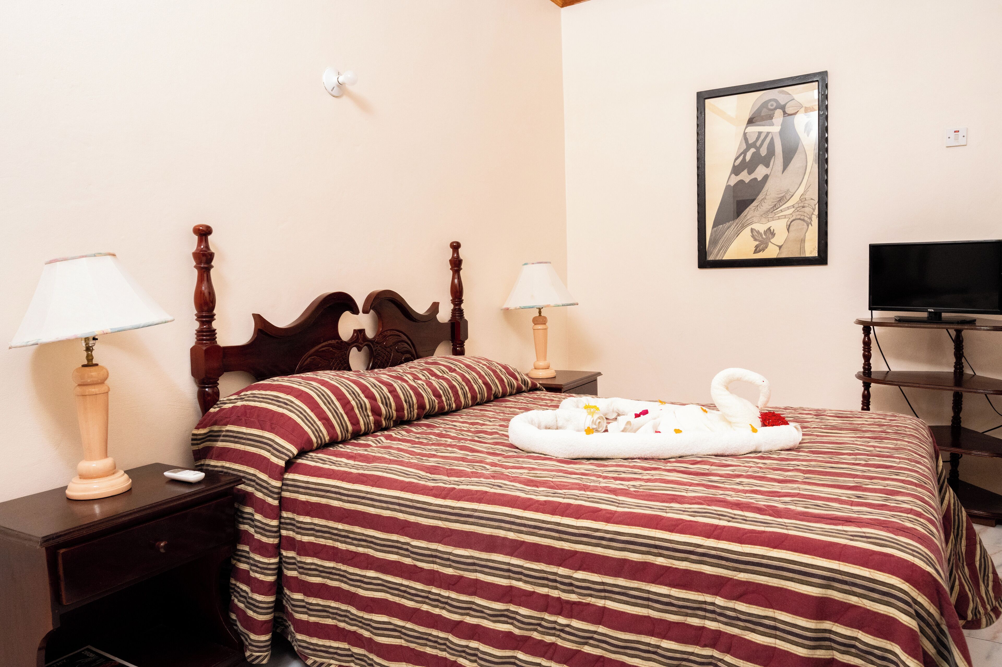 A hotel room with a wooden bed, striped bedding, two bedside lamps, a flat-screen TV, and a framed artwork on the wall.