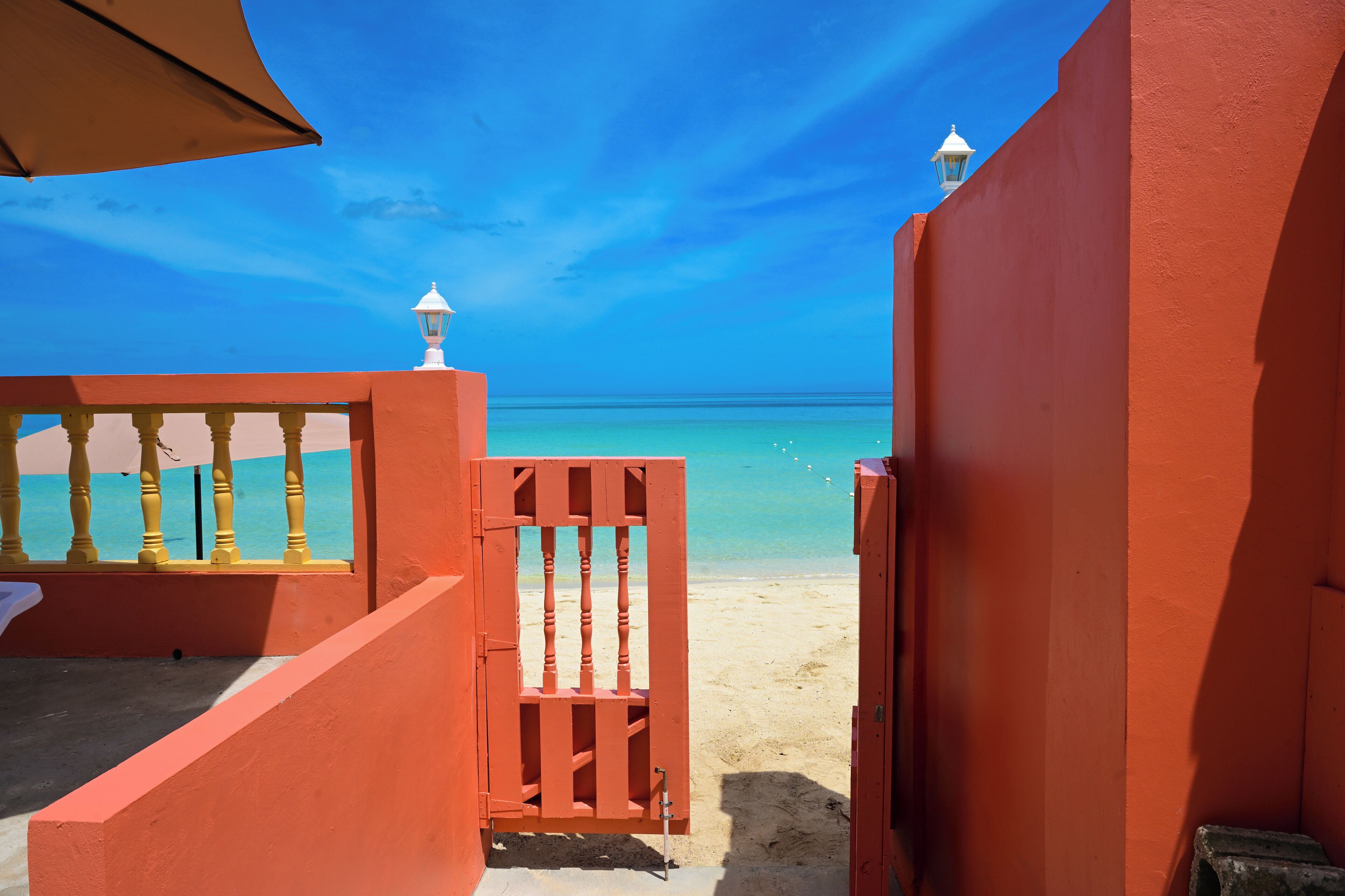 Vista da praia com um portão vermelho e um lampião branco.