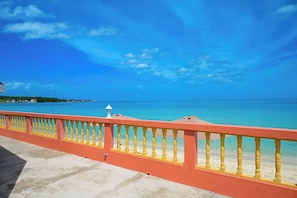 Vista costeira com corrimão vermelho, céu azul límpido e mar calmo.