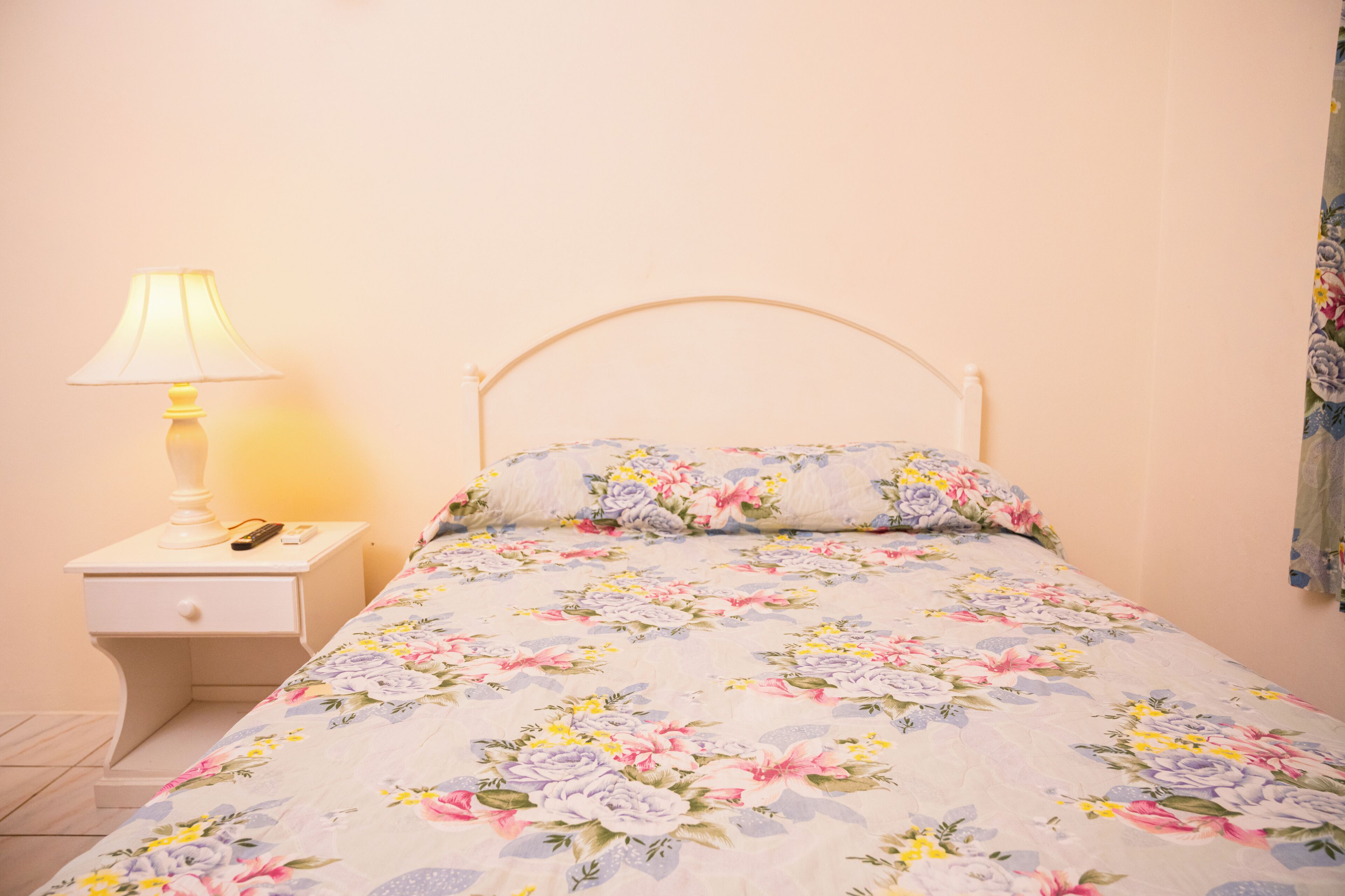 A bed with a floral bedspread, a bedside lamp, and a nightstand with a remote control.