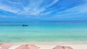 A beach with clear turquoise water, a boat in the distance, and beach umbrellas.