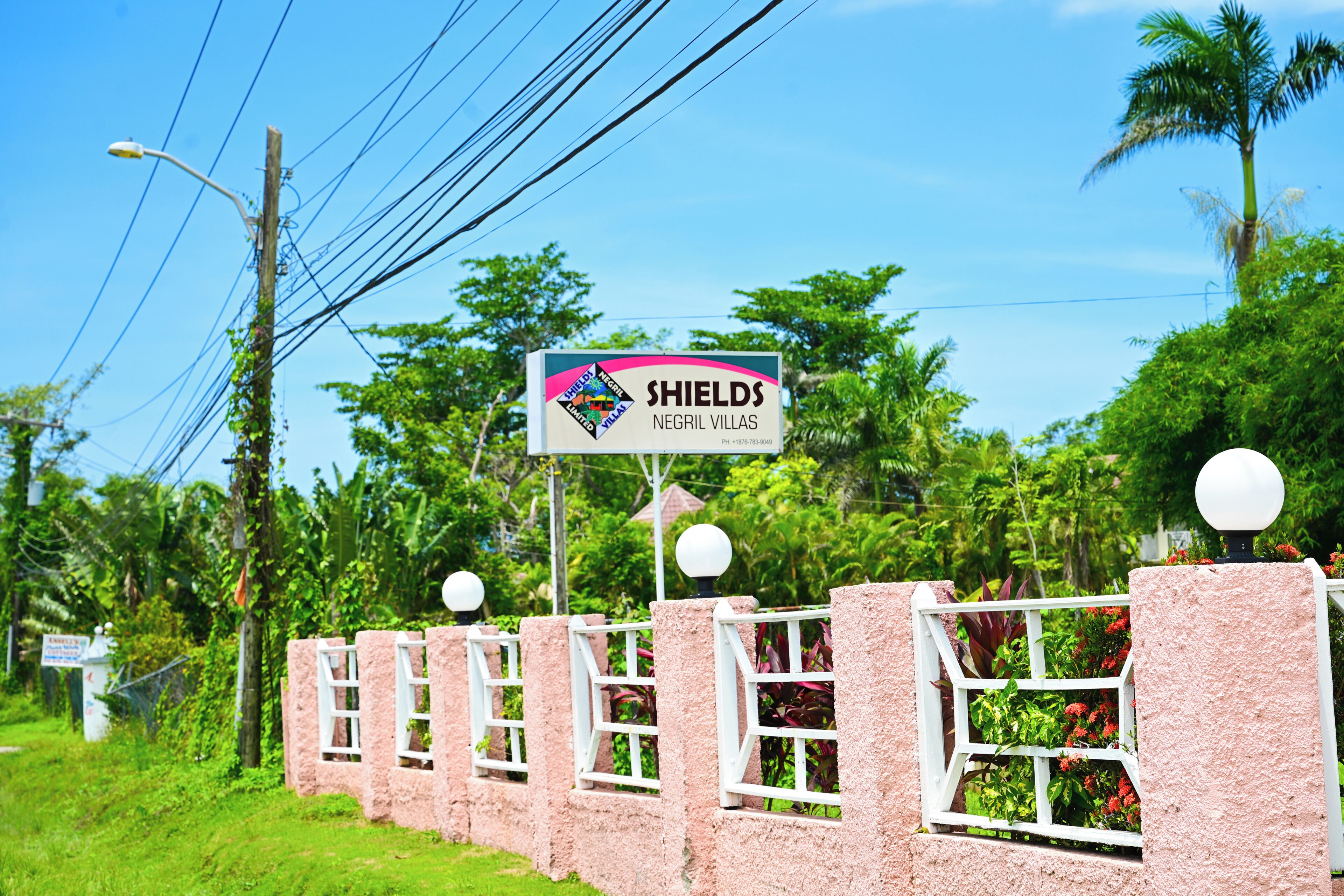 A sign for 'SHIELDS NEGRIL VILLAS' with a white fence and decorative spheres.