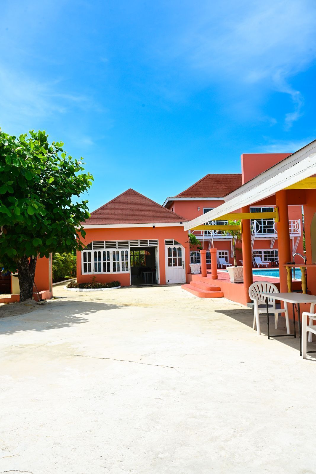Ein Gebäude mit roter Fassade, einer überdachten Terrasse mit weißen Stühlen und einem Pool.