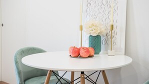 Une table ronde blanche, une chaise de couleur turquoise, un vase avec des fleurs blanches et trois pommes.