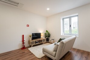 Relax in this stylish living room with a sofa against a window offering a view of the outdoors, a flat-screen TV, and a potted plant.