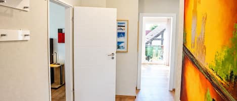 Un pasillo con una puerta blanca, un banco, un cuadro y vistas al exterior.